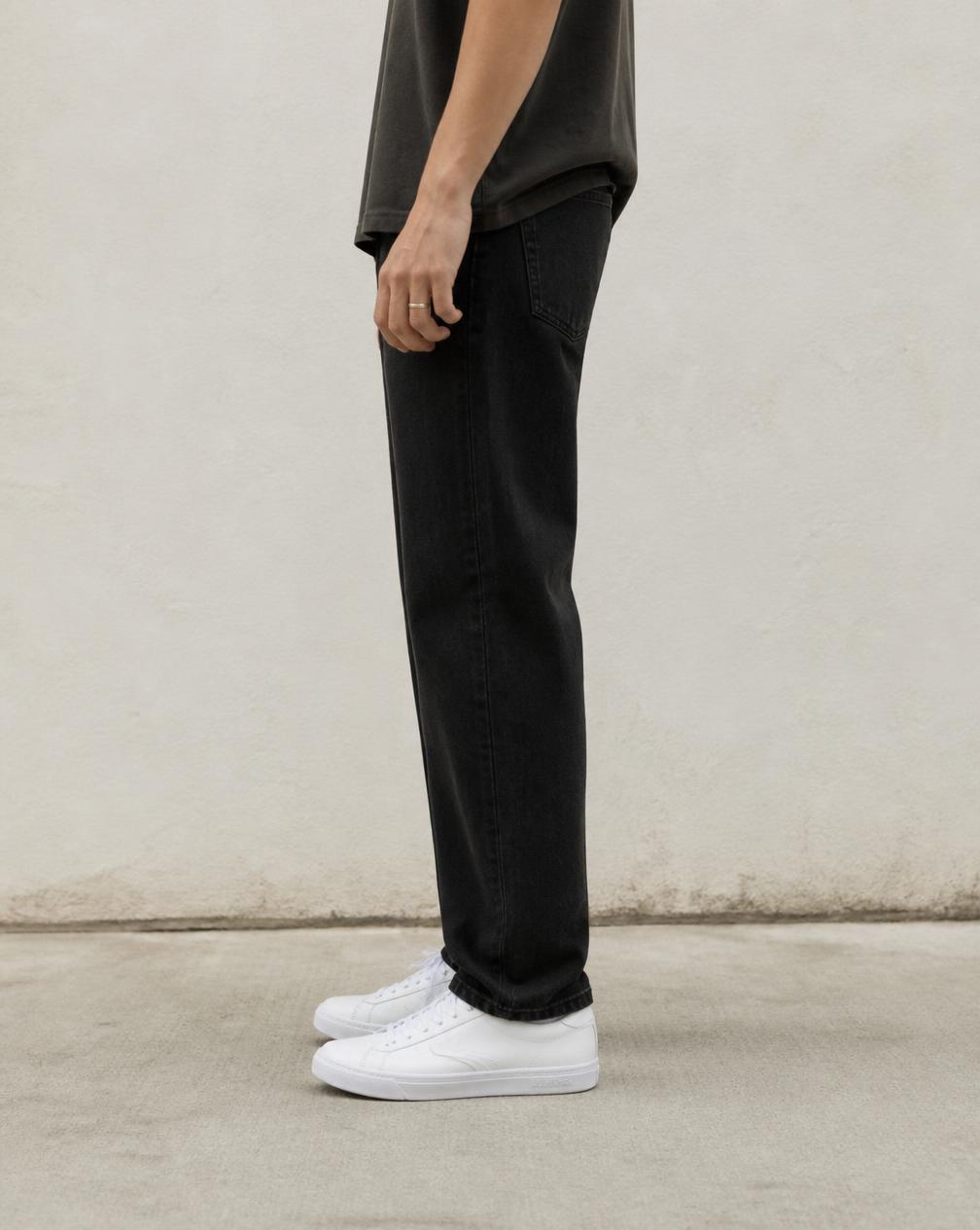 Side profile of legs in black jeans and white sneakers on concrete